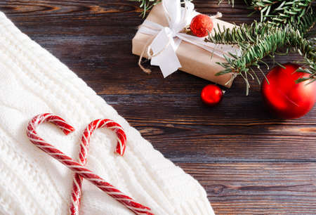 lollipops on a white sweater, spruce branch, red Christmas balls, gift box on a wooden background