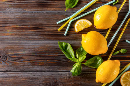several, 3 yellow whole lemons and slices, sprigs of green Basil, yellow tubes on a dark wooden background close upの写真素材