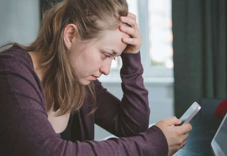 1 white european young blonde woman in a maroon jacket with a gadget in the roomの写真素材