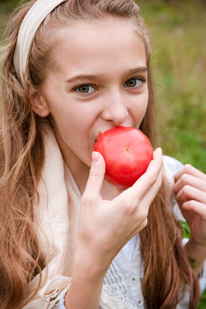 1 white girl 11 years old eats a fresh red tomatoの写真素材
