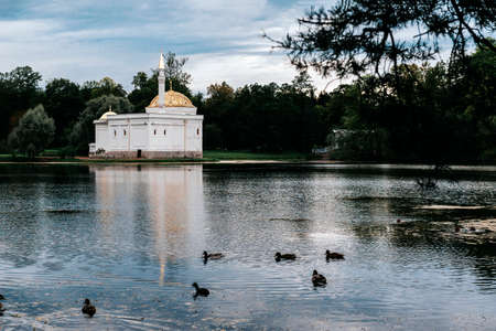 white pavilion in Oriental style in a Park on the Bank of a pond with ducks on a background of greenery on a cloudy day, Saint Petersburgの写真素材