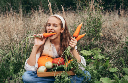 1 white girl 11 years old sitting on the grass and eating fresh carrots, fresh apples, cucumbers,...
