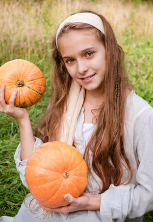 1 white girl 11 years old holding 2 ripe round orange pumpkins on a green backgroundの写真素材