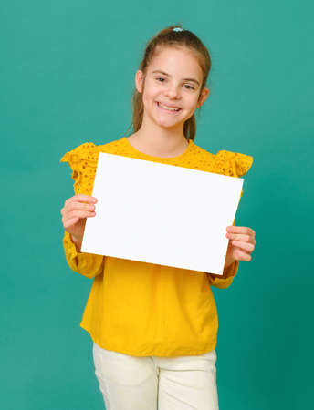 1 white teenage girl 10 years old in a yellow blouse holding a white sign and smiling on a green backgroundの写真素材