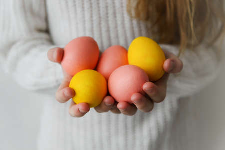 girl in a white sweater holds yellow and pink Easter eggs in her hands