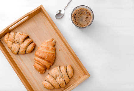 glass of black coffee, 3 croissants on a tray, a spoon on a white background top view, breakfastの写真素材