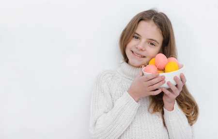 a10 year old European girl with pink and yellow Easter eggs in her hands, wearing a white sweater against a white wallの写真素材