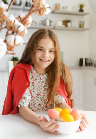 European girl 10 years old smiles in the kitchen at the table with Easter eggs
