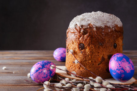 pink and purple eggs, willow twigs, Easter cake with icing and raisins on a dark wooden background