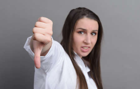 1 white young woman in a white shirt shows a sign with her finger down, bad on a gray backgroundの写真素材