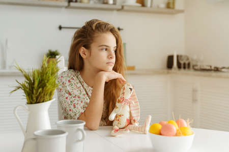 european girl 10 years old in the kitchen at the table with Easter eggs and a toy rabbit