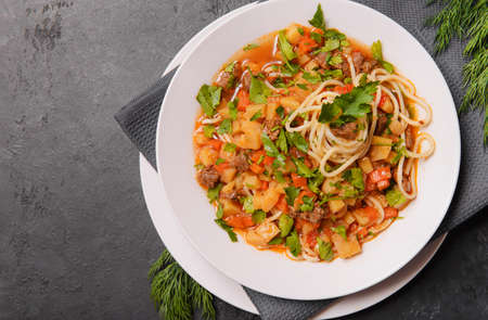 Caucasian lagman with meat, vegetables and homemade noodles, greens on a dark background, national home cookingの写真素材