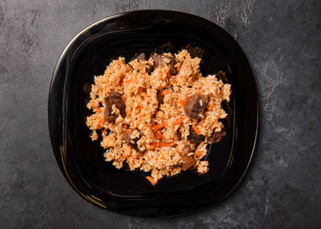meat Uzbek pilaf with meat on a black plate on a dark background top view