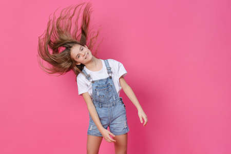 white girl 10 years old in a white top waving long hair, having fun on a pink background, emotions, childの写真素材