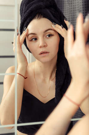 white young woman with a black towel in the bathroom in front of the mirrorの写真素材