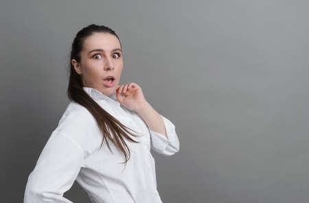 white young woman in white shirt surprised, scared on gray background
