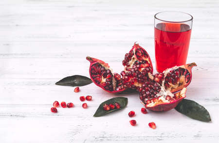 ripe red pomegranate, a glass of juice on a white wooden backgroundの写真素材