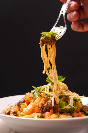 plate with a lagman fork with pasta, meat, sauce and herbs on a dark background, Caucasian Asian cuisineの写真素材