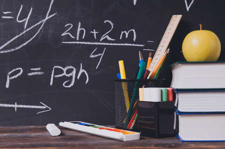 formulas, chalk inscriptions on a blackboard, books, pens, apples, markers, on the table,の写真素材