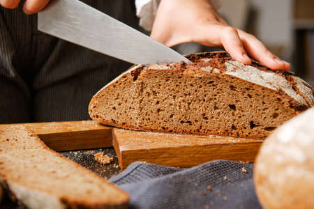 man cuts rye bread with a knife on a board