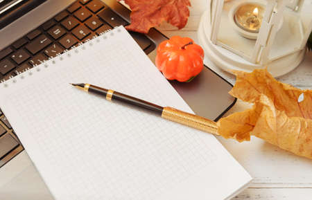 autumn composition, pen, notebook, pumpkin, laptop, leaves, candle on a white table,の写真素材