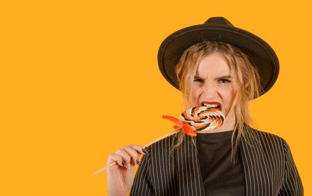 Young girl posing on yellow background with lollipop direct look biting brown clothes copy space...
