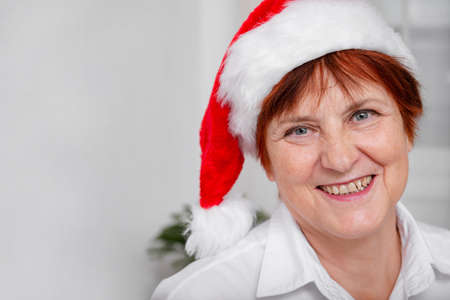Old woman red hair in santa's hat on white background in white shirt horizontal minimalistic copy space close up smilingの写真素材