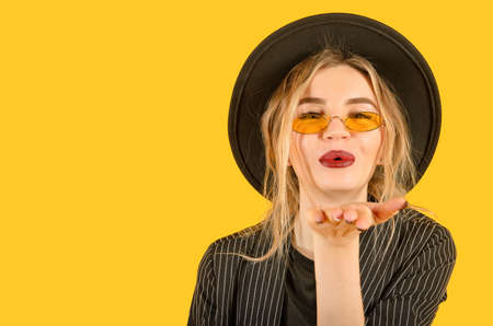 Young girl posing on yellow background direct look air kiss close up brown clothes yellow glasses copy space minimalisticの写真素材