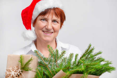 Old woman in santa's hat with present and tree branches close up with white backgroundの写真素材