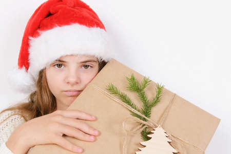 Young girl in white sweater and silver santa hat holds present christmas close horizontal simple background minimalistic holidaysの写真素材