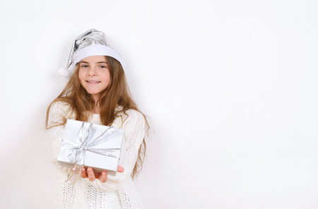 Young girl in white sweater and silver santa hat holds present christmas smile simple background minimalistic holidaysの写真素材