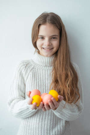 Young girl smiling holds easter colorful eggs white background sweater brown hair spring warm cozy...