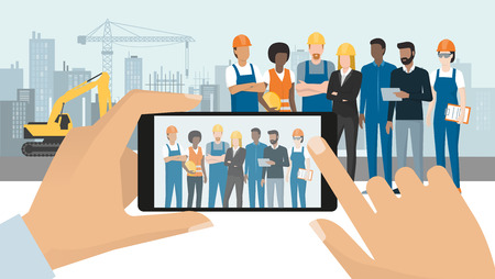 Professional construction workers and engineers posing together on the contruction site, a man is taking a picture with a smartphone, subjective point of viewのイラスト素材