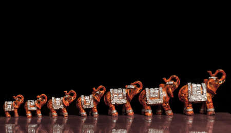 Toy models of elephants standing in a row on black background.の写真素材