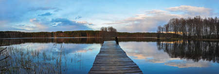 Panorama landscape. Wooden pier on the lake at sunset, clouds reflection in the waterの写真素材