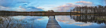 Panorama landscape. Wooden pier on the lake at sunset, clouds reflection in the waterの写真素材