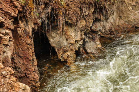 Grotto in a red rock on a mountain river. Altai, Russia.