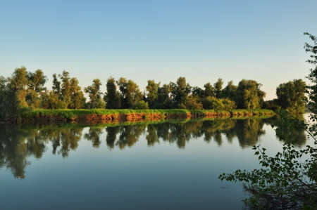 Tranquil nature scene. Water surface and green shores of the river Ob in soft evening sunset colors....
