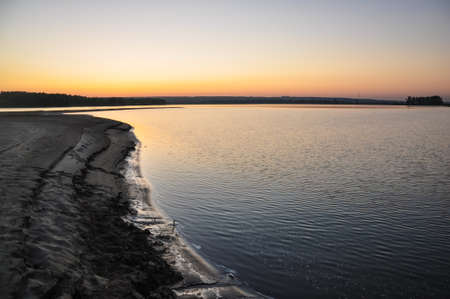 Tranquil nature scene. Sunset dawn sky above the sandy beach and water surface of the river Ob in...