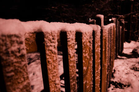 Snow covered rural wooden fence in the night illuminated by warm street lightの写真素材