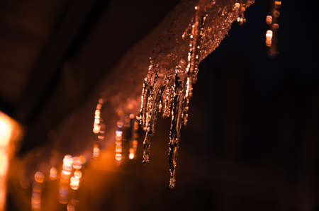 Icicles illuminated by warm street light in the night against dark sky.の写真素材