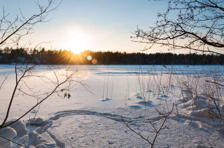 Beautiful winter scene. Sunset at the frozen lake covered with snowの写真素材