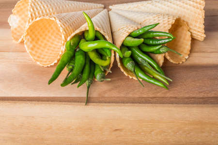 Green hot chili peppers in wafer cones on wooden backgroundの写真素材
