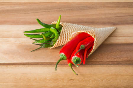 Red and green hot chili peppers in wafer cones on wooden backgroundの写真素材