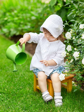 on a summer day, a little girl takes care of flowers in the garden, watering roses in a flower bedの写真素材