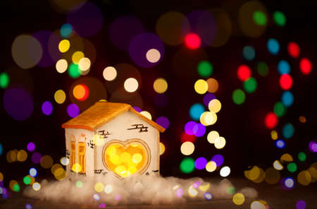 fairy tale toy gingerbread house on a wooden Board and a dark background with a bokeh of lights garlandsの写真素材