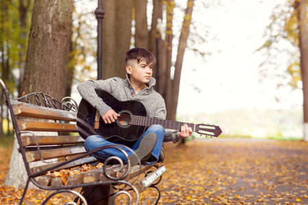 a teenage street musician plays a black acoustic guitar on an autumn day in the Parkの写真素材
