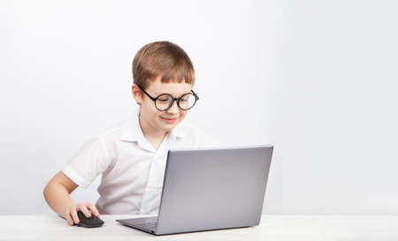 a boy with glasses, an elementary school student, sits at a table with a laptop on a white backgroundの写真素材