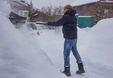 a man cleans the road from snow with a shovel, winter morning, snowfall