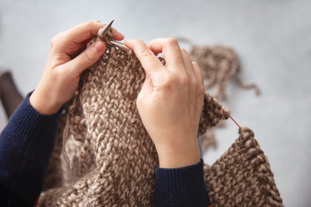 a woman is sitting by the window knitting a sweater made of thick thread